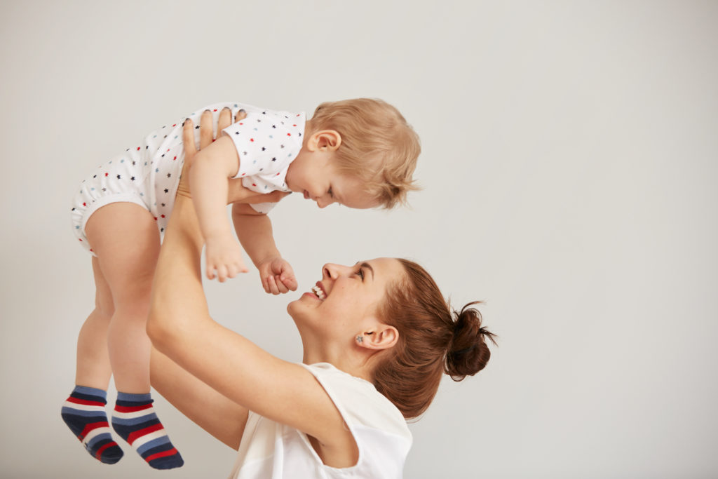 Young mother playing with her little baby on the bed - indoors