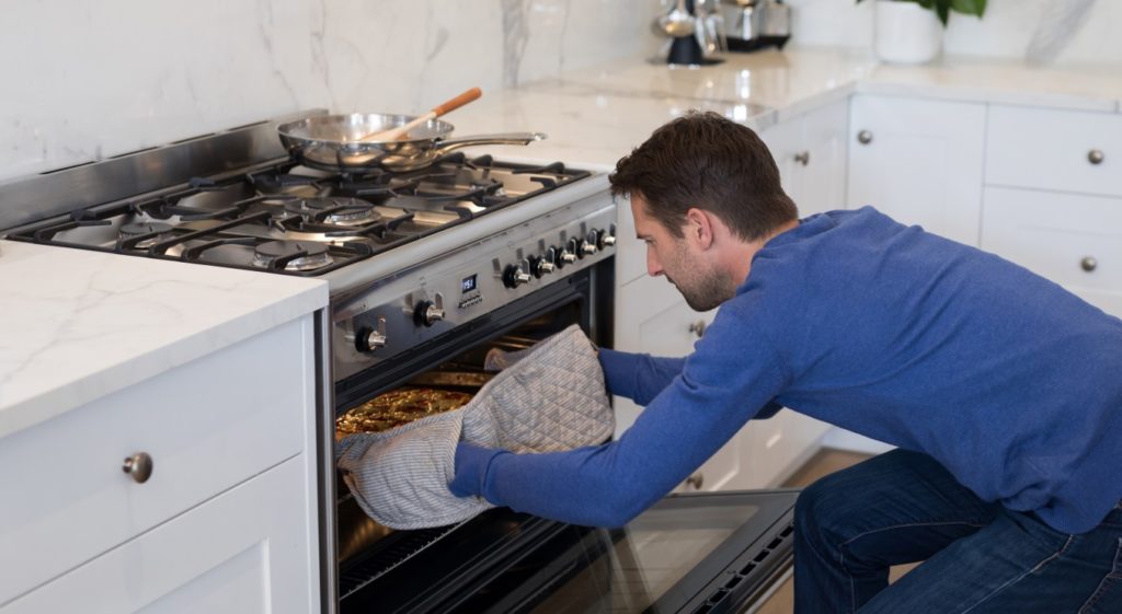 Man putting pizza into oven in kitchen at home