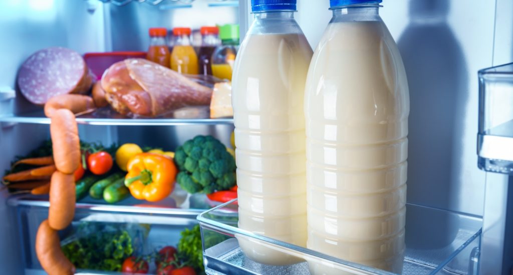 Open refrigerator filled with food. Focus on Bottles of milk in the fridge