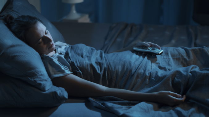 Woman sleeping with her TV on, she is holding the remote control